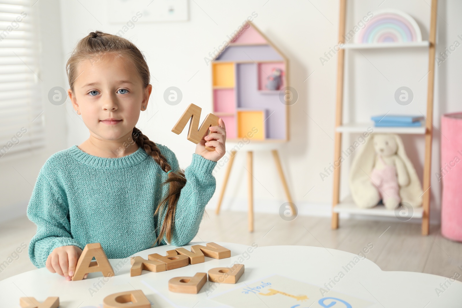 Photo of Little girl learning alphabet with wooden letters at white table indoors