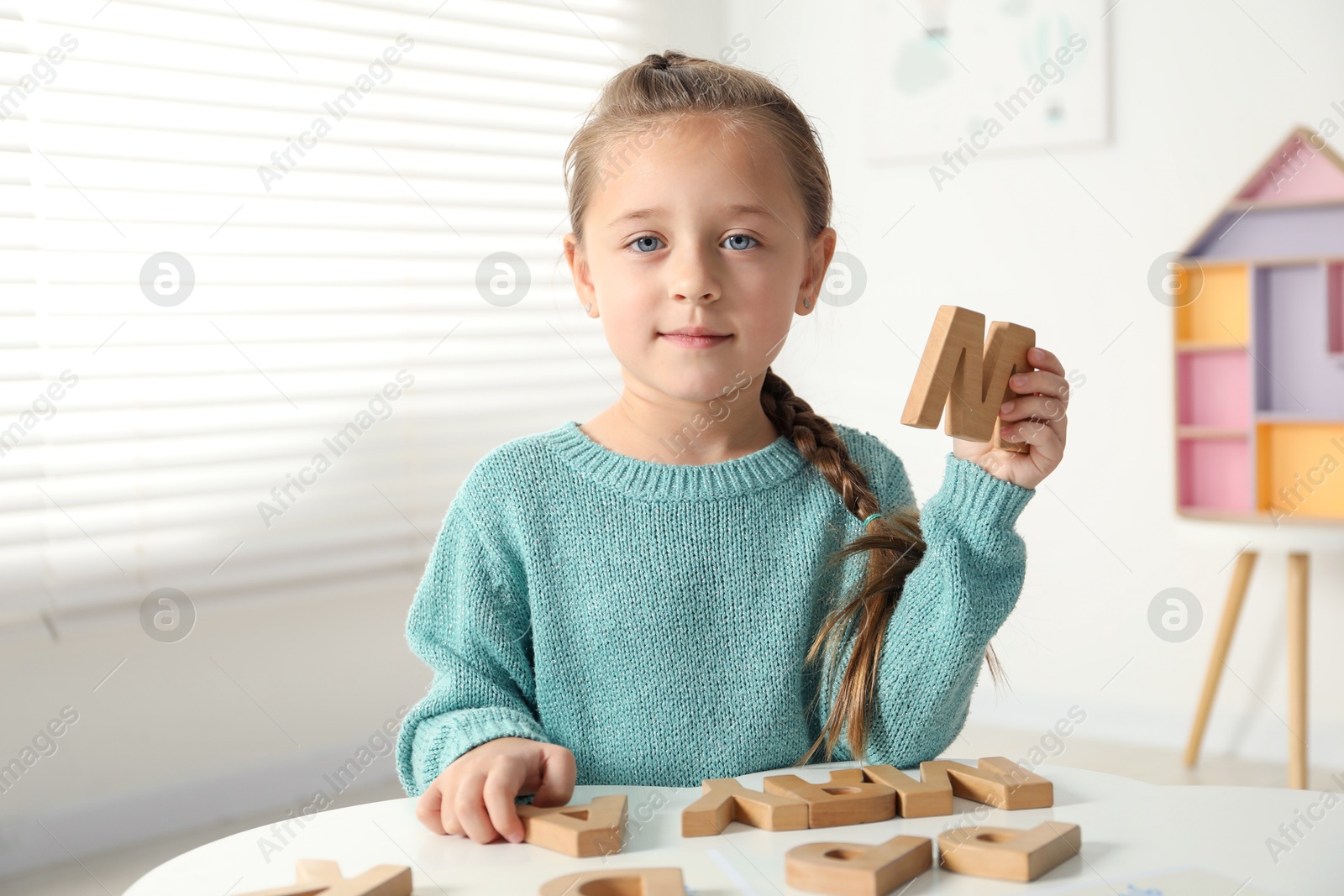 Photo of Little girl learning alphabet with wooden letters at white table indoors