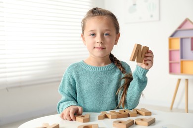 Photo of Little girl learning alphabet with wooden letters at white table indoors