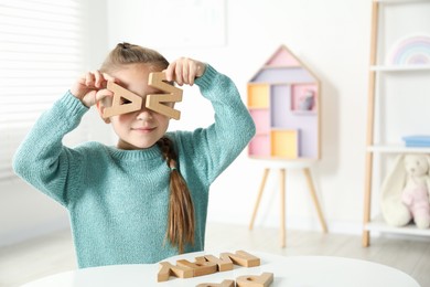 Photo of Little girl learning alphabet with wooden letters at white table indoors