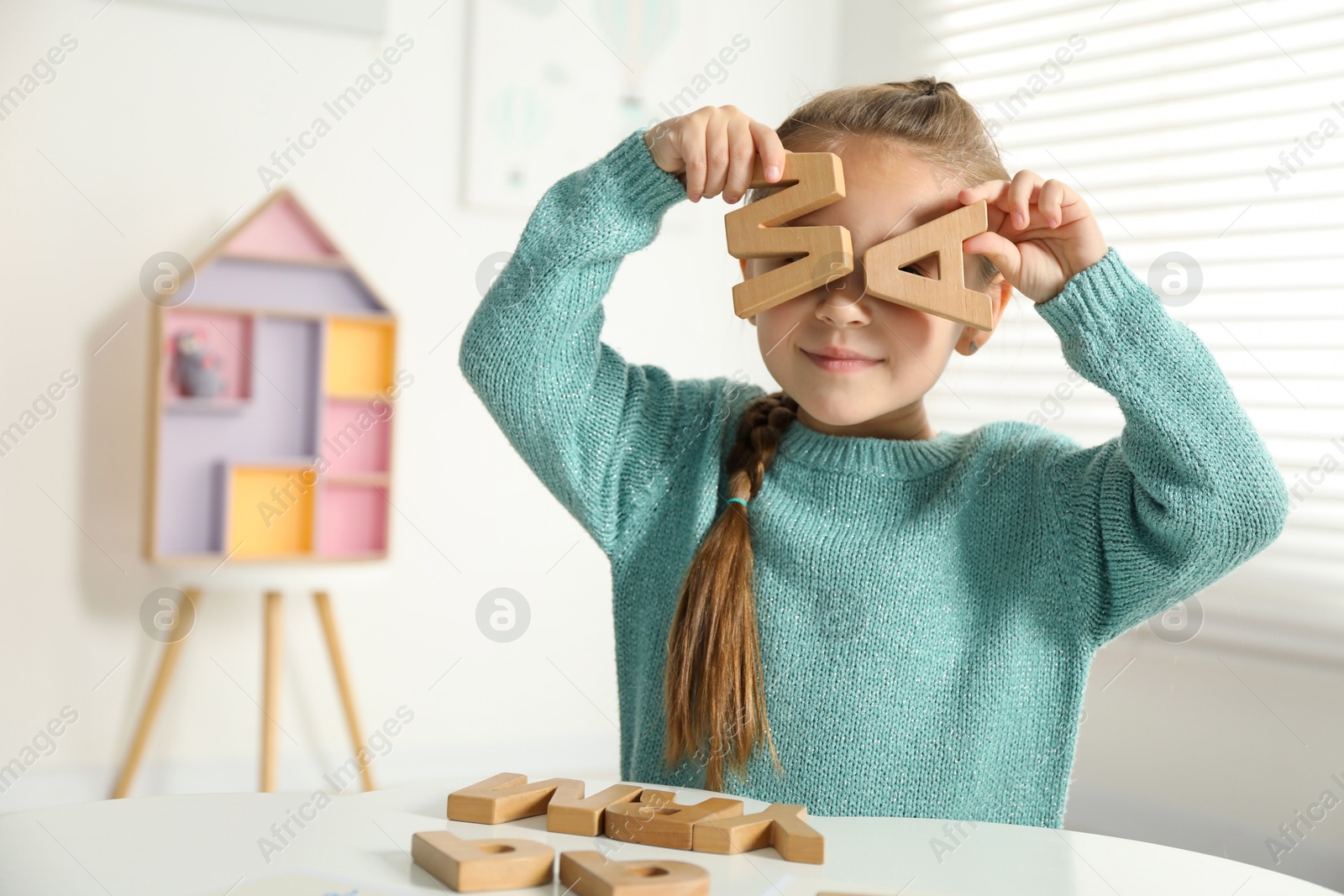 Photo of Little girl learning alphabet with wooden letters at white table indoors