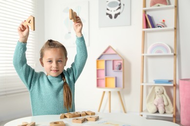 Photo of Little girl learning alphabet with wooden letters at white table indoors