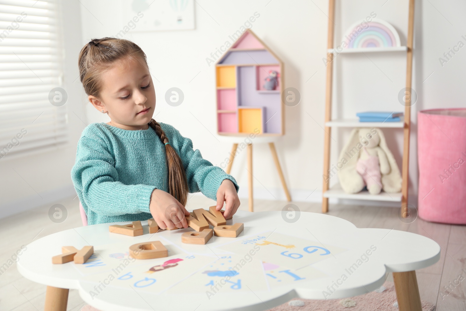 Photo of Little girl learning alphabet with wooden letters at white table indoors