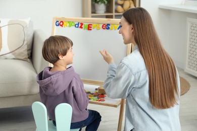 Photo of Speech therapist teaching little boy alphabet with magnetic letters indoors