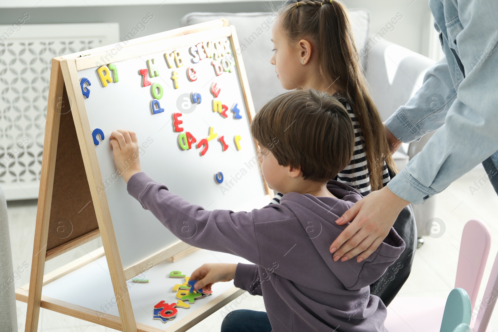 Photo of Speech therapist teaching little kids alphabet with magnetic letters indoors, closeup