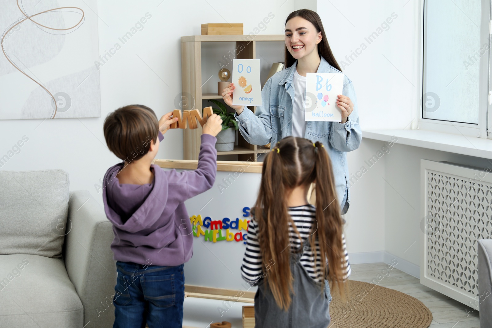 Photo of Speech therapist teaching little kids alphabet indoors