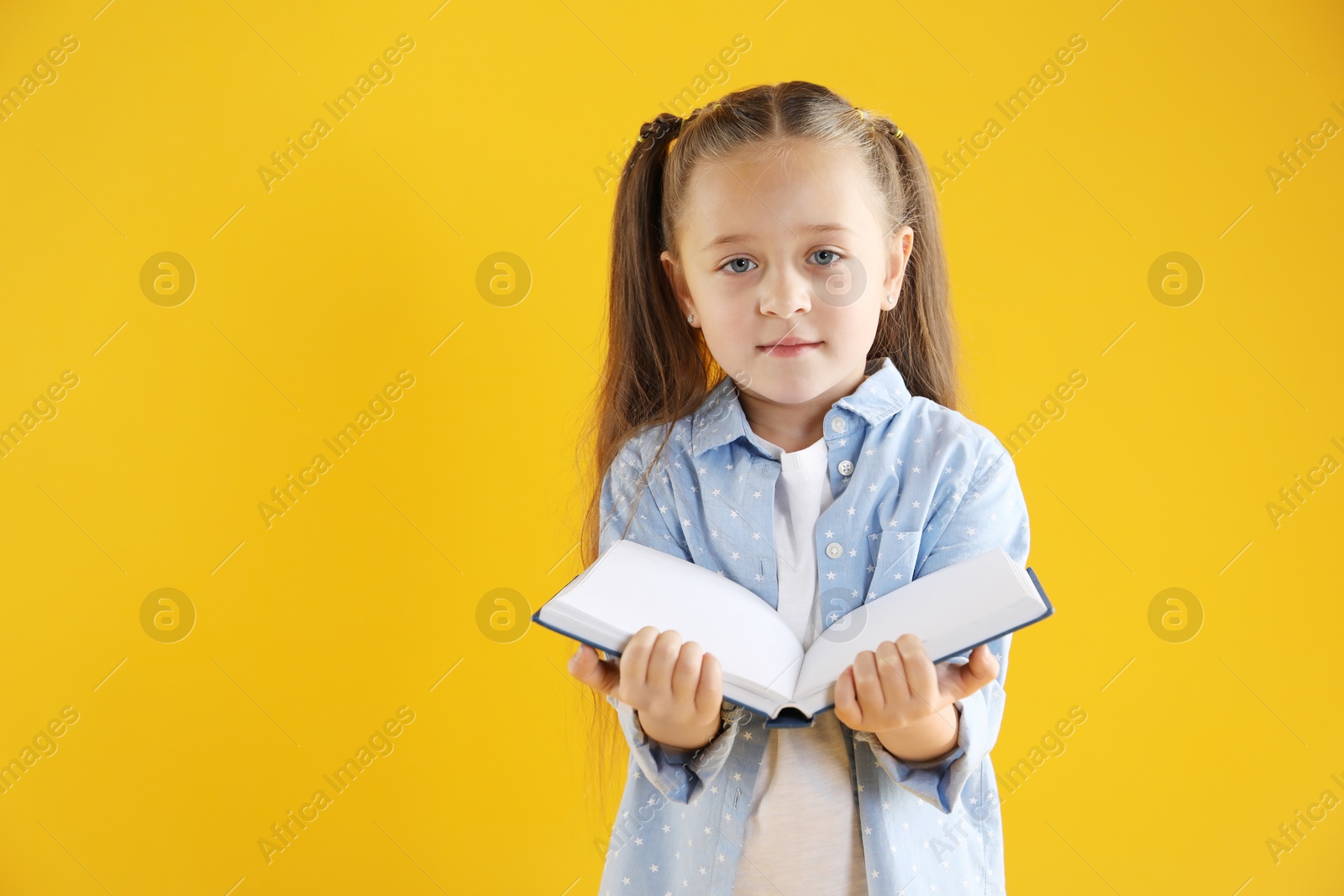 Photo of Learning alphabet. Little girl with book on orange background, space for text