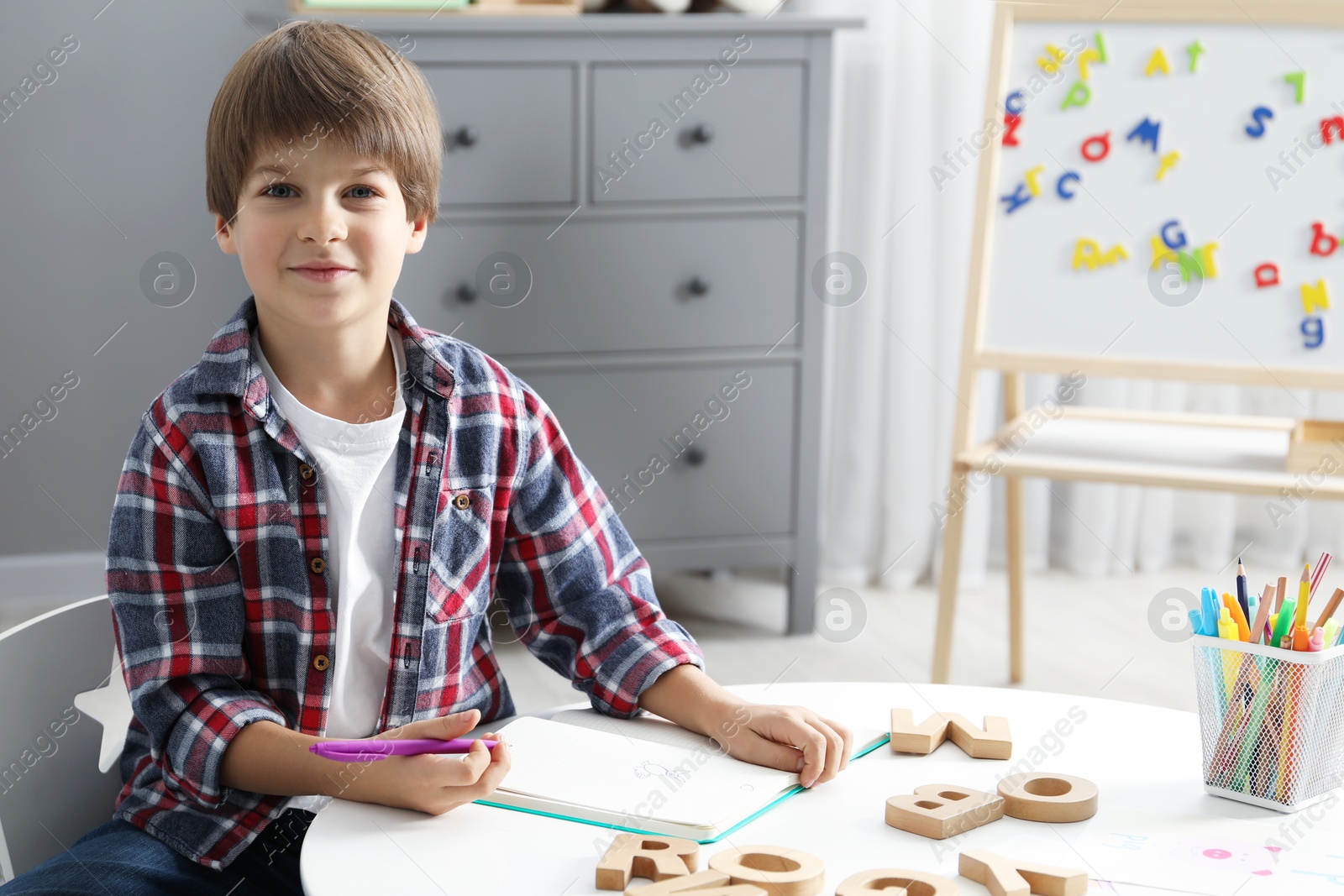 Photo of Little boy learning alphabet at white table indoors