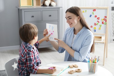 Photo of Speech therapist teaching little boy alphabet at white table indoors