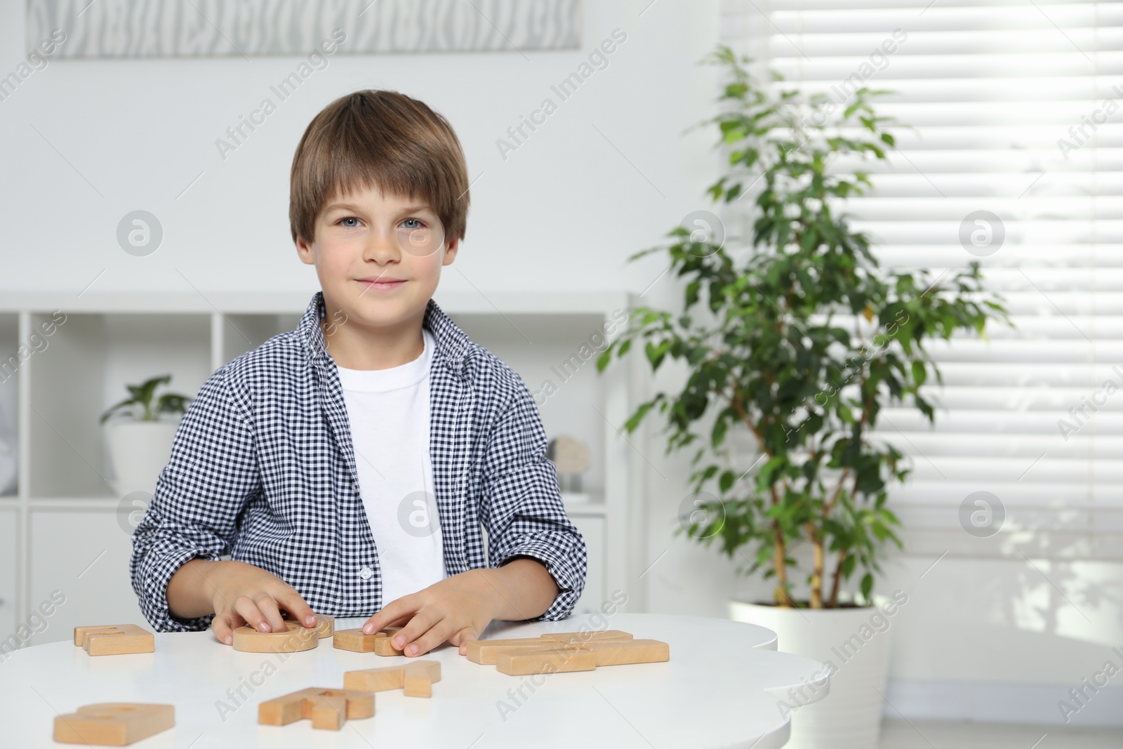 Photo of Little boy learning alphabet with wooden letters at white table indoors