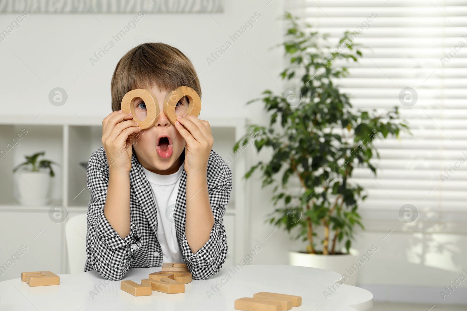 Photo of Little boy learning alphabet with wooden letters at white table indoors