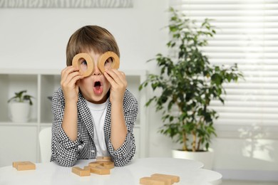 Photo of Little boy learning alphabet with wooden letters at white table indoors