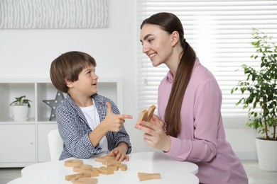 Photo of Speech therapist teaching little boy alphabet with wooden letters at white table indoors