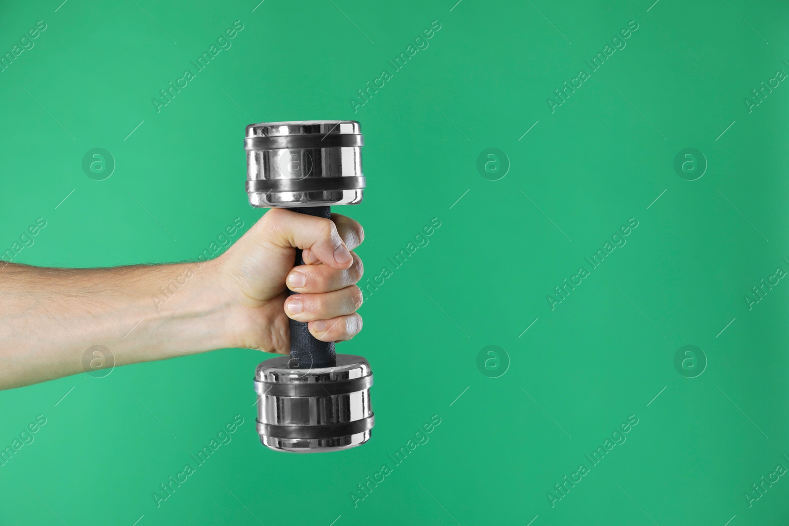 Photo of Man exercising with dumbbell on green background, closeup. Space for text