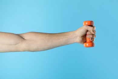 Photo of Man exercising with dumbbell on light blue background, closeup