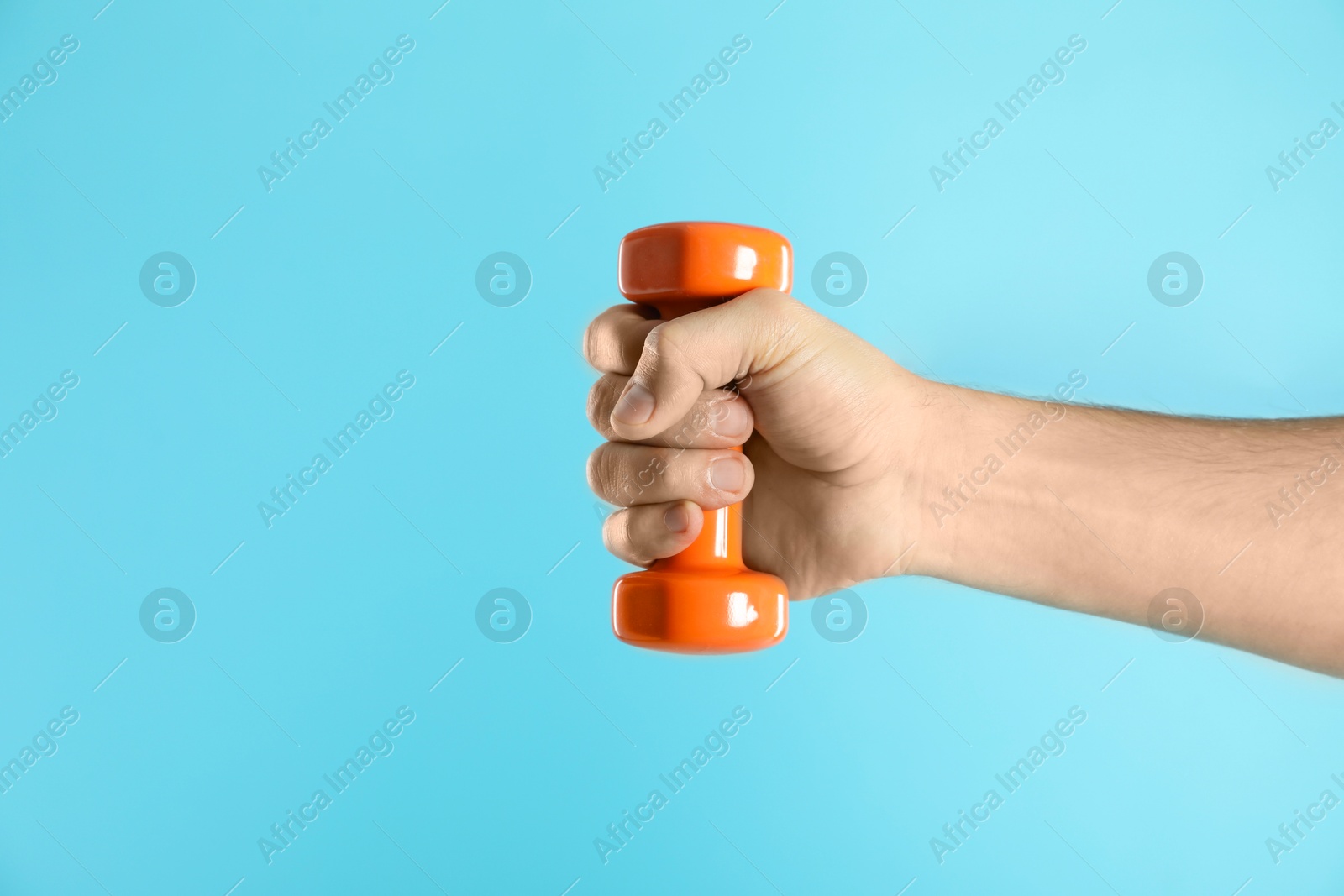 Photo of Man exercising with dumbbell on light blue background, closeup. Space for text