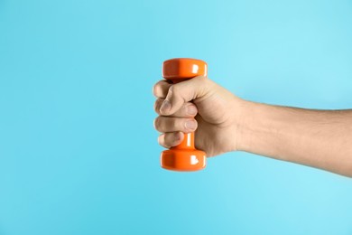 Photo of Man exercising with dumbbell on light blue background, closeup. Space for text