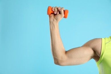 Photo of Man exercising with dumbbell on light blue background, closeup. Space for text