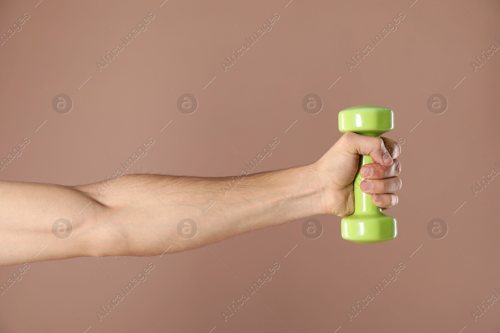 Photo of Man exercising with dumbbell on light brown background, closeup