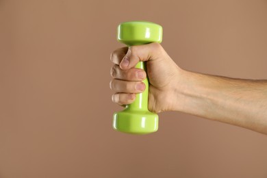 Photo of Man exercising with dumbbell on light brown background, closeup