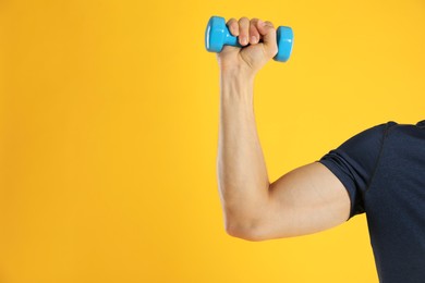 Photo of Man exercising with dumbbell on yellow background, closeup. Space for text