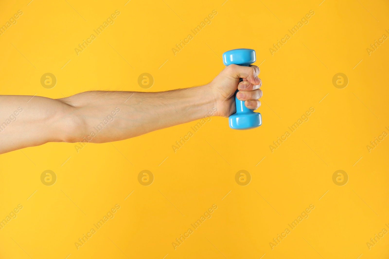 Photo of Man exercising with dumbbell on yellow background, closeup