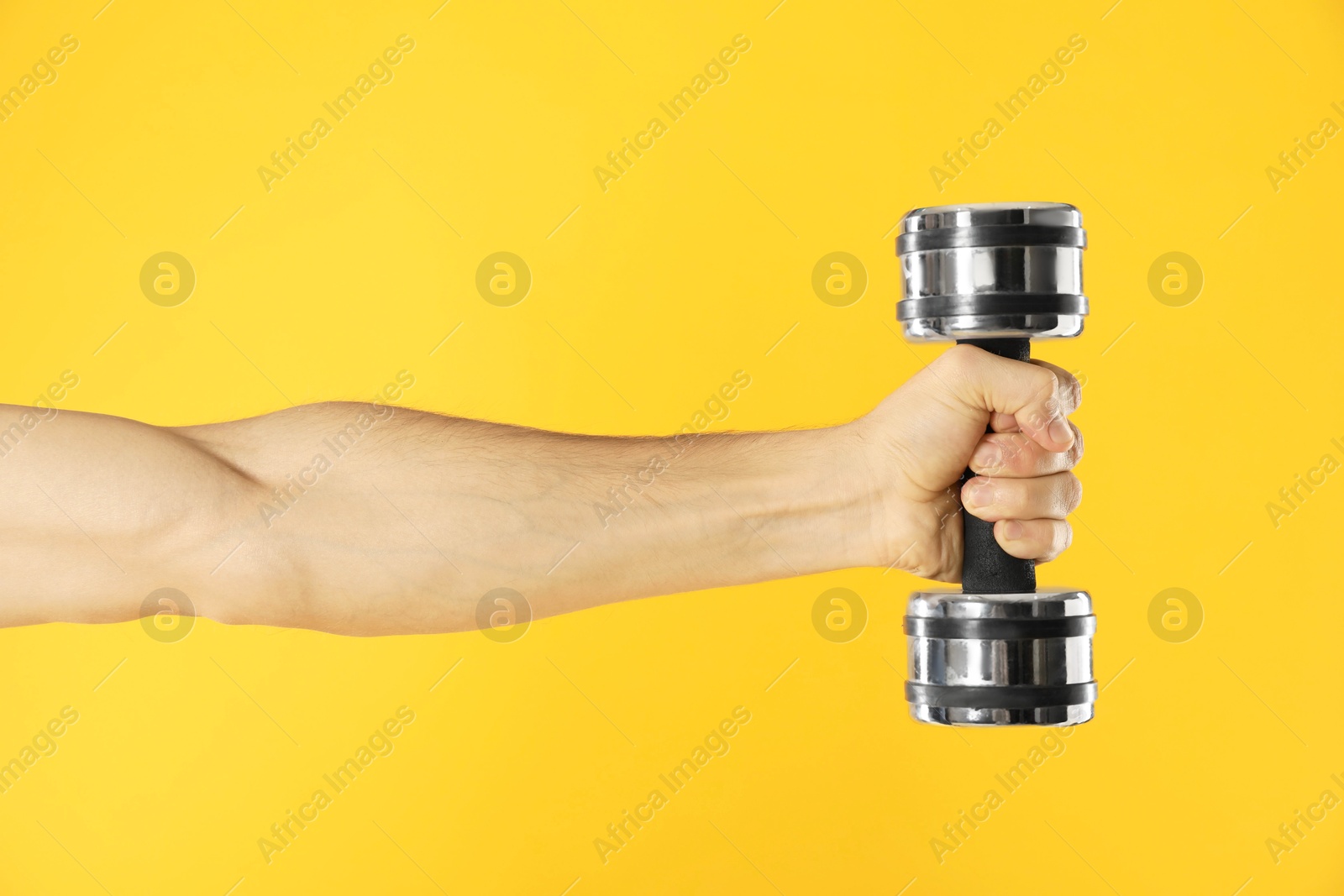 Photo of Man exercising with dumbbell on yellow background, closeup