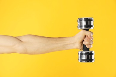 Photo of Man exercising with dumbbell on yellow background, closeup