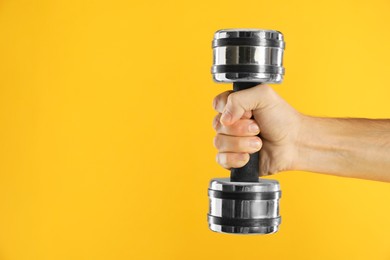 Photo of Man exercising with dumbbell on yellow background, closeup. Space for text