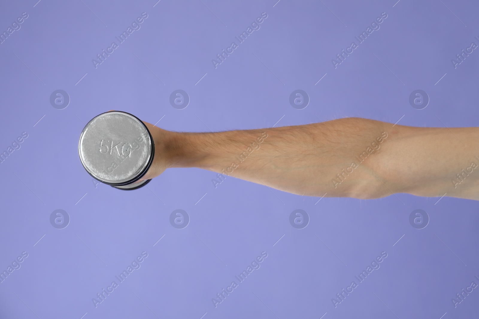 Photo of Man exercising with dumbbell on violet background, closeup