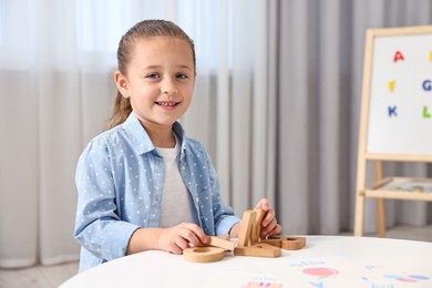 Photo of Little girl learning alphabet with wooden letters at white table indoors