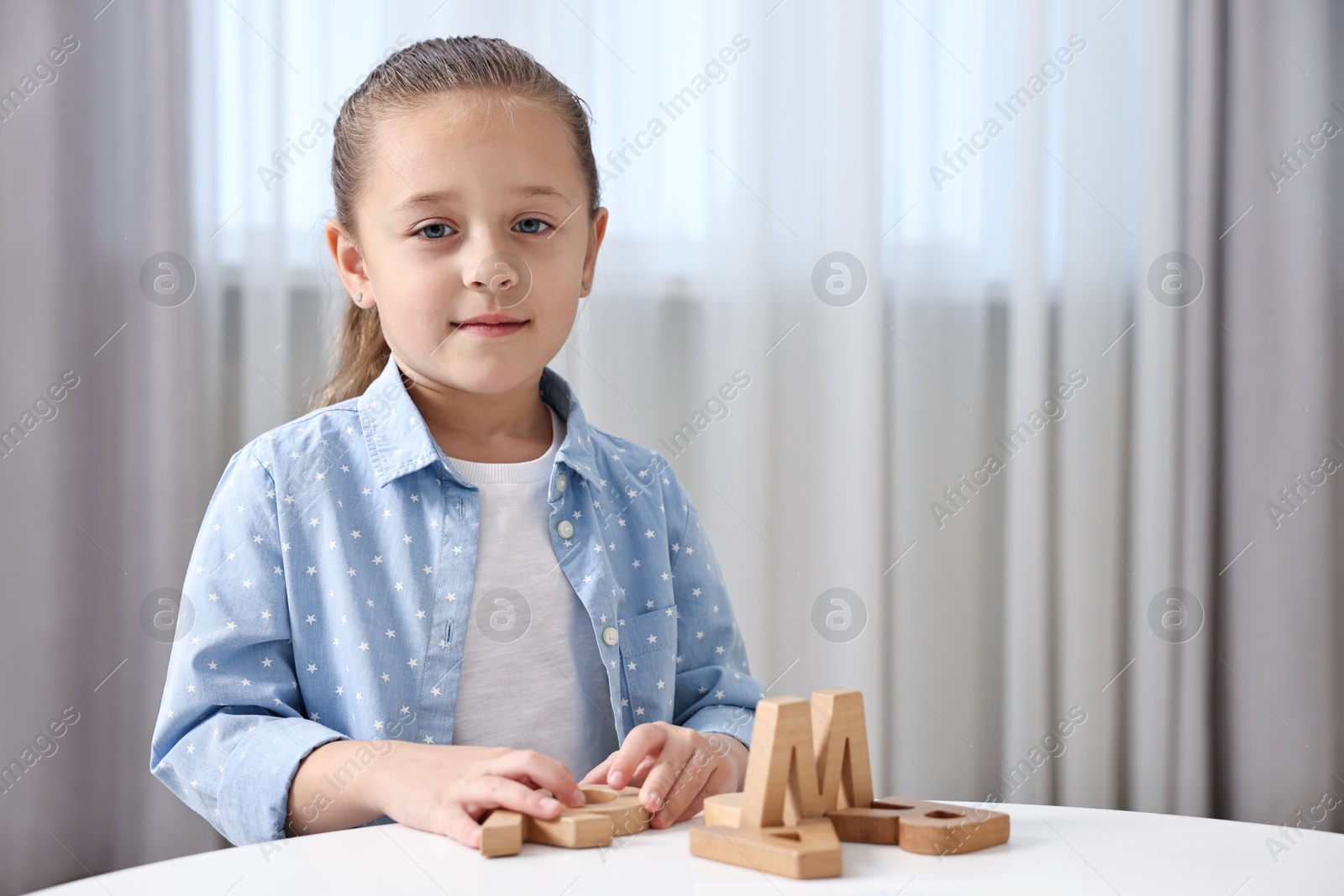 Photo of Little girl learning alphabet with wooden letters at white table indoors, space for text