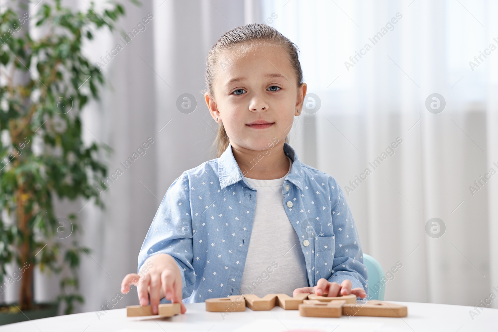 Photo of Little girl learning alphabet with wooden letters at white table indoors