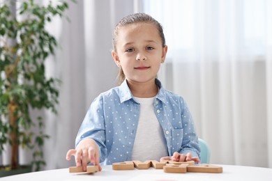 Photo of Little girl learning alphabet with wooden letters at white table indoors