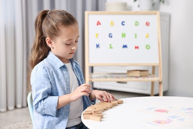 Photo of Little girl learning alphabet with wooden letters at white table indoors