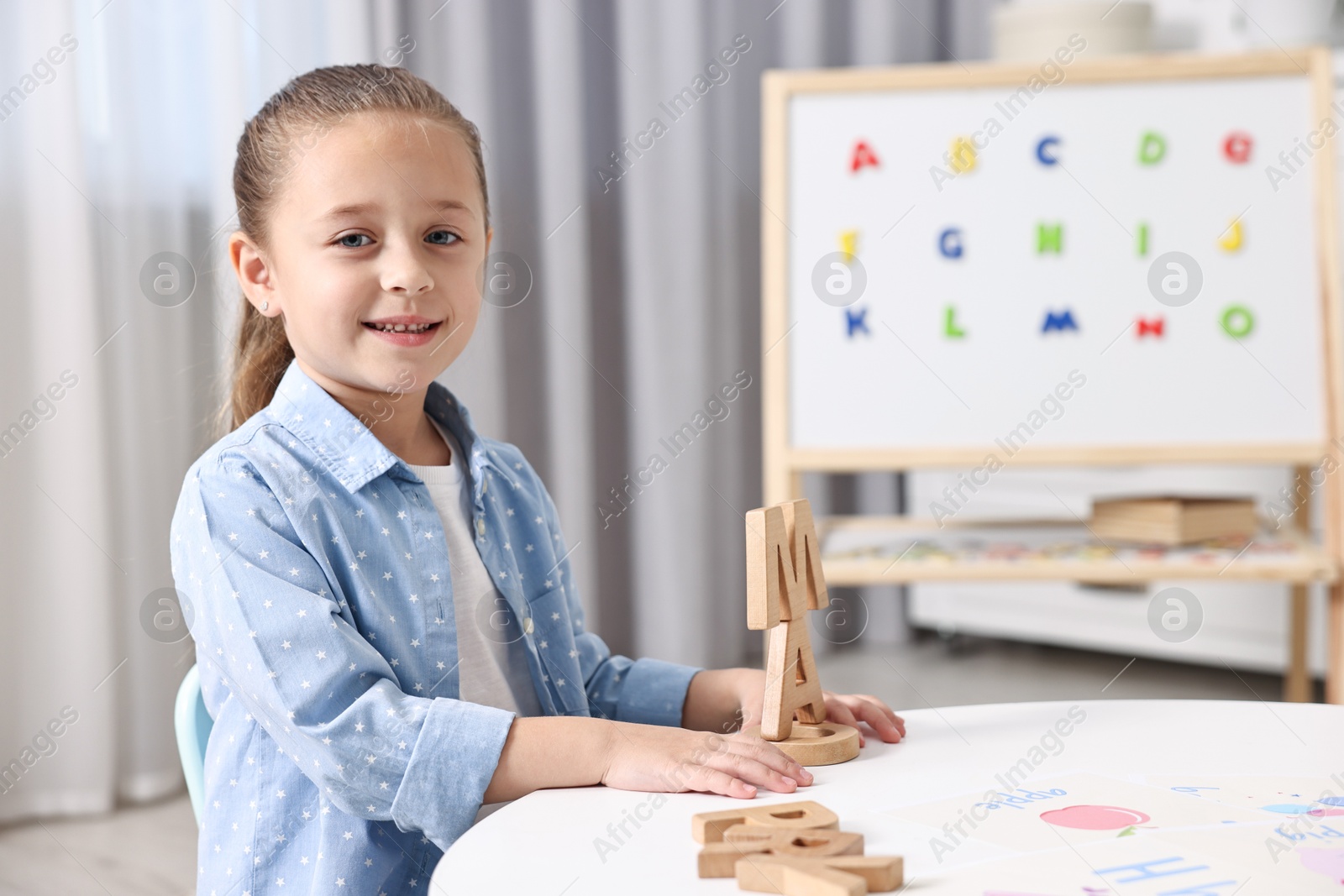 Photo of Little girl learning alphabet with wooden letters at white table indoors