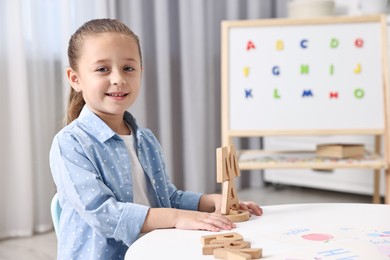 Photo of Little girl learning alphabet with wooden letters at white table indoors