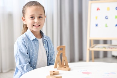 Photo of Little girl learning alphabet with wooden letters at white table indoors