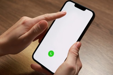 Photo of Woman dialing number on smartphone at wooden table, closeup