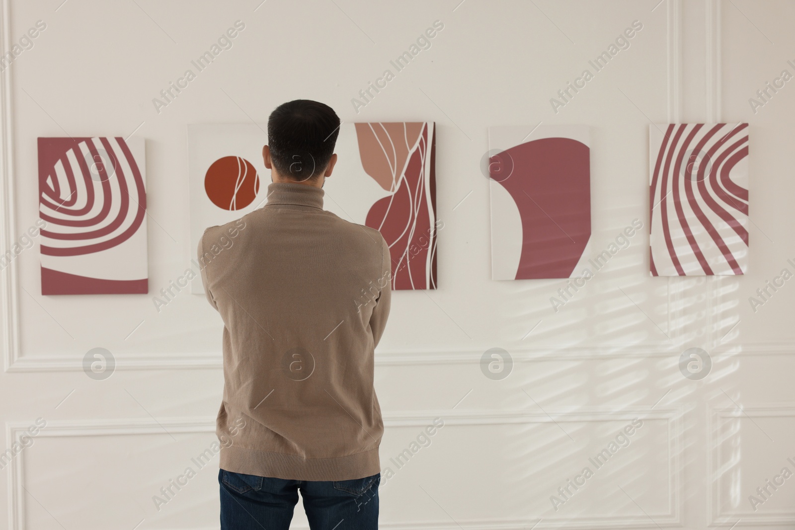 Photo of Man studying beautiful artwork in modern gallery, back view