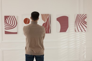 Photo of Man studying beautiful artwork in modern gallery, back view