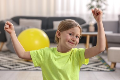 Cute little girl showing her biceps indoors