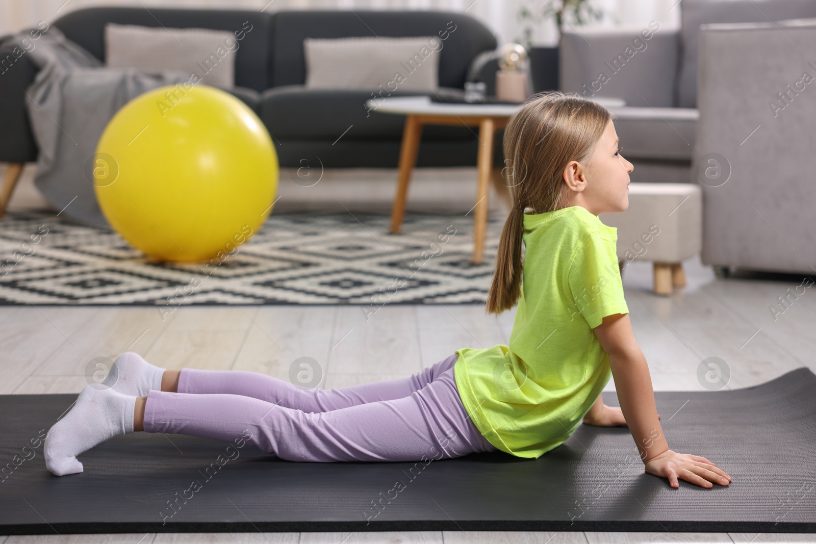 Photo of Cute little girl exercising on fitness mat indoors