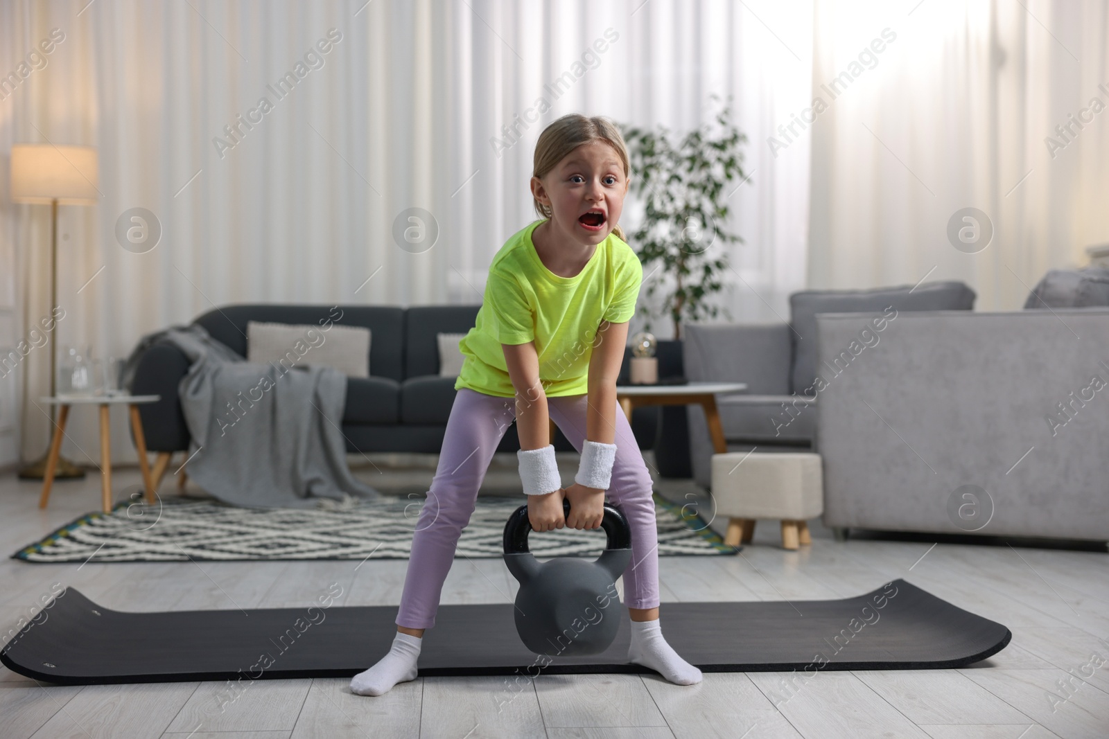 Photo of Cute little girl exercising with kettlebell indoors