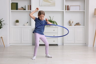 Photo of Cute little girl exercising with hula hoop indoors