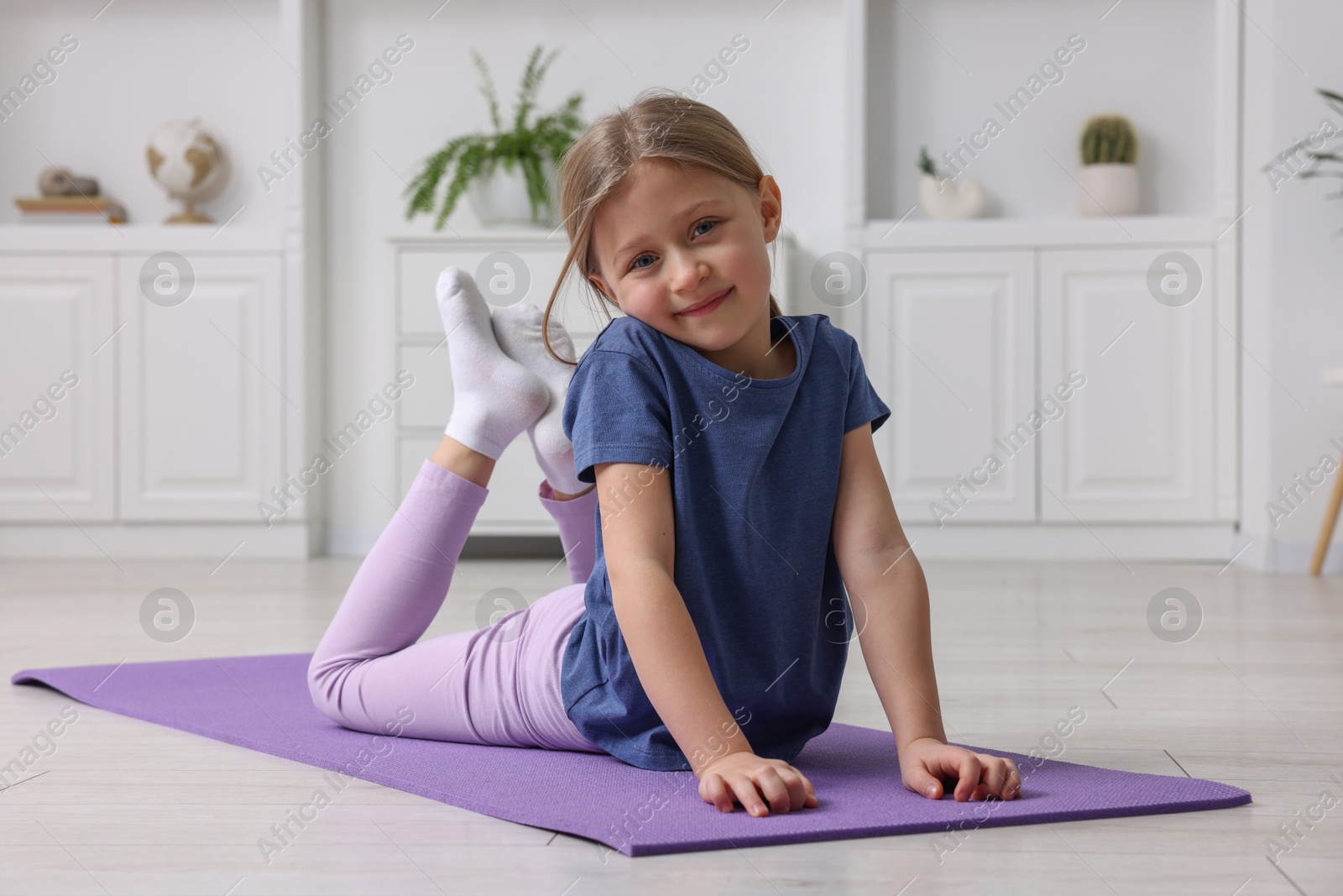 Photo of Cute little girl exercising on fitness mat indoors