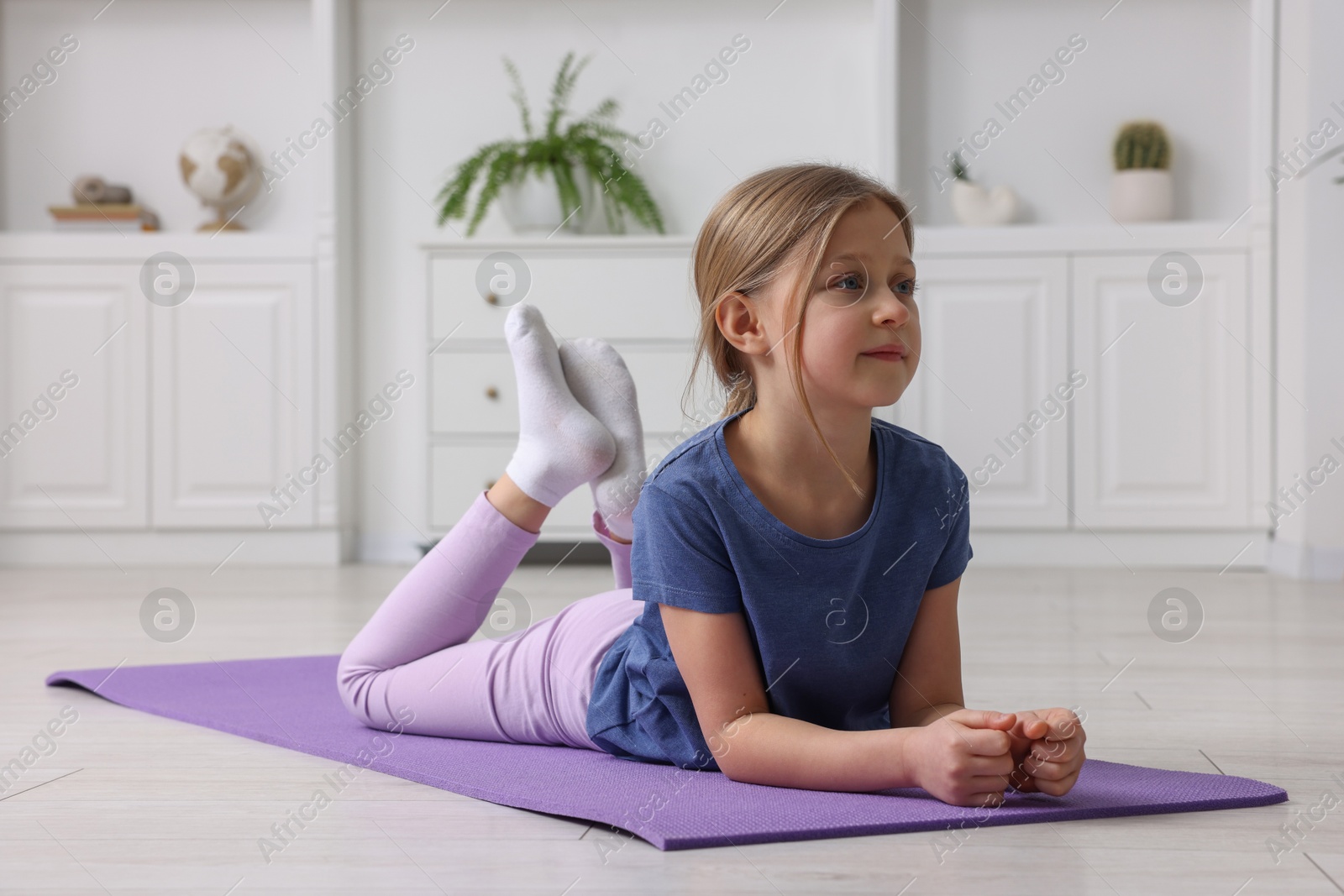 Photo of Cute little girl exercising on fitness mat indoors