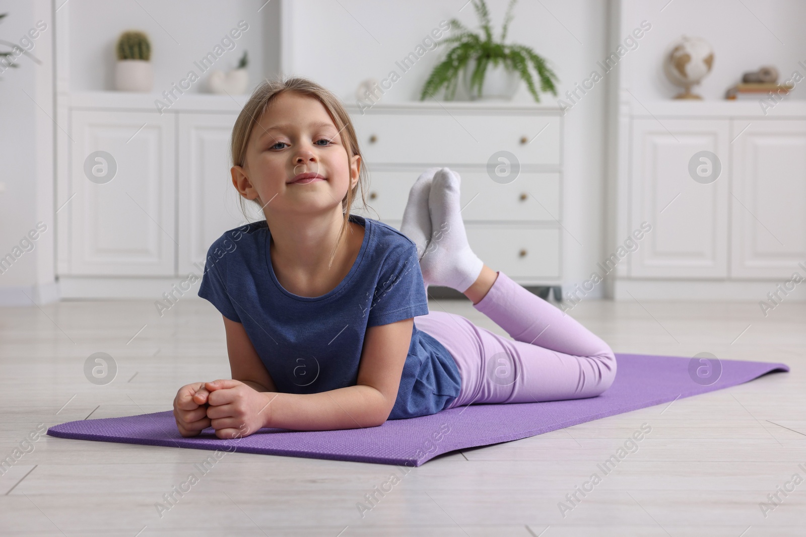 Photo of Cute little girl exercising on fitness mat indoors