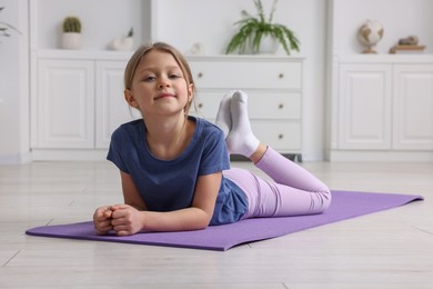 Photo of Cute little girl exercising on fitness mat indoors