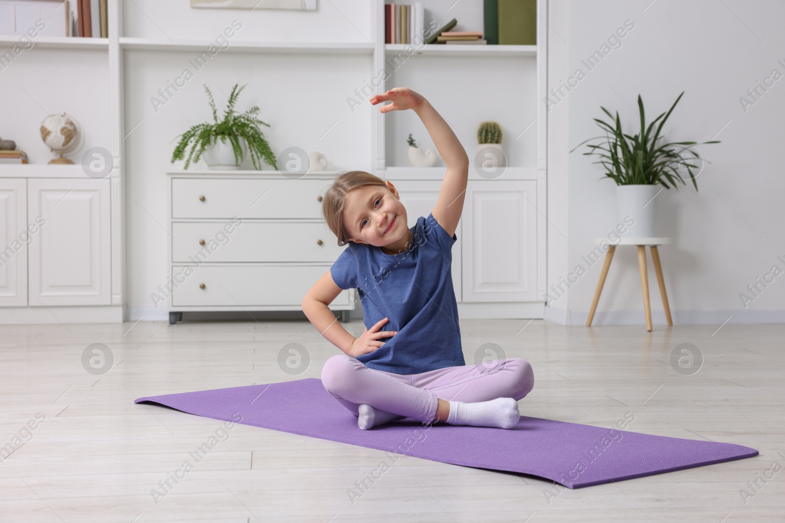 Photo of Cute little girl exercising on fitness mat indoors